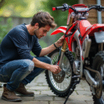 Jeune homme nettoyant la chaîne d'une moto motocross de 150 cc